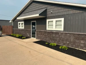Narrow black mulch bed with new plantings along the foundation of a dark sided building