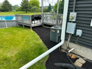Black mulch bed edged around an air conditioning unit beside a backyard pool deck