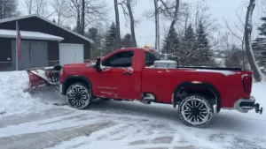 Red pickup fitted with a snow plow blade parked in the snow beside a shed in Laingsburg, Michigan